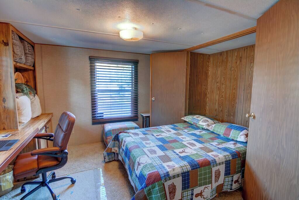 A bedroom with a wooden desk, two beds, and a window with blinds.