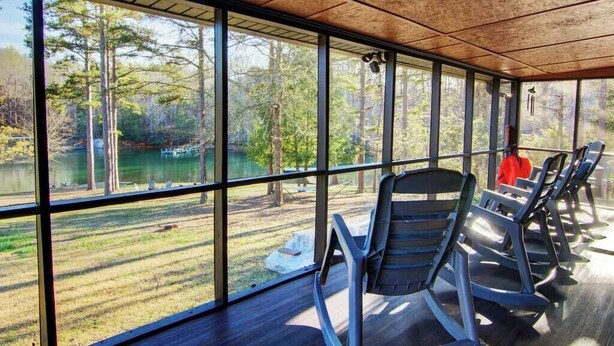Un área de estar al aire libre con techo, con grandes ventanales que dan a un lago y un bosque.