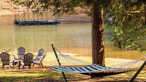 Una hamaca, sillas y una mesa junto a un lago, con un puente al fondo.