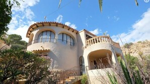 Eine Villa im mediterranen Stil mit einer gewölbten Fassade, Bogenfenstern und einem Balkon mit Geländer.