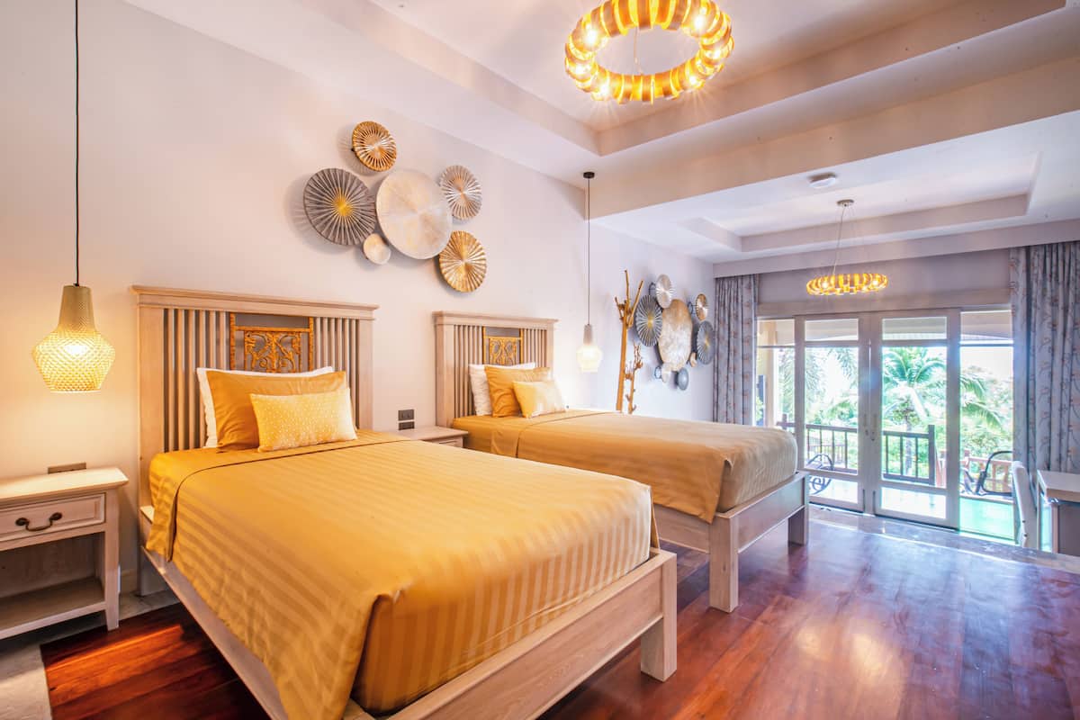 A hotel room with two beds, wooden headboards, and a large window with a view of palm trees.