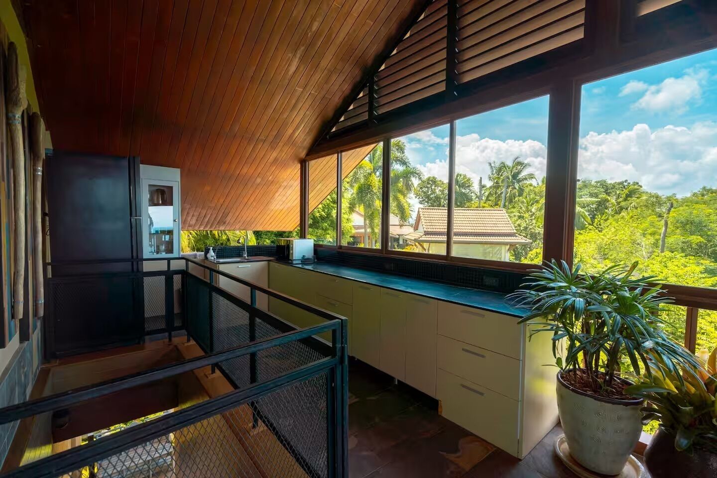 A modern kitchen with a view of lush greenery and a house.