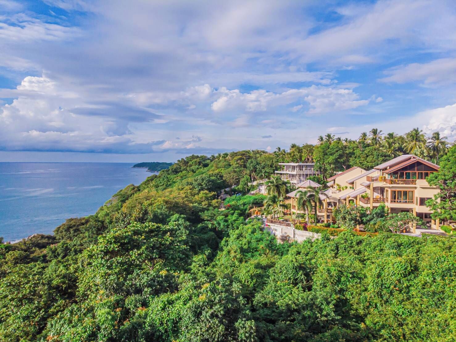 A coastal resort with multiple buildings, lush greenery, and a view of the sea.