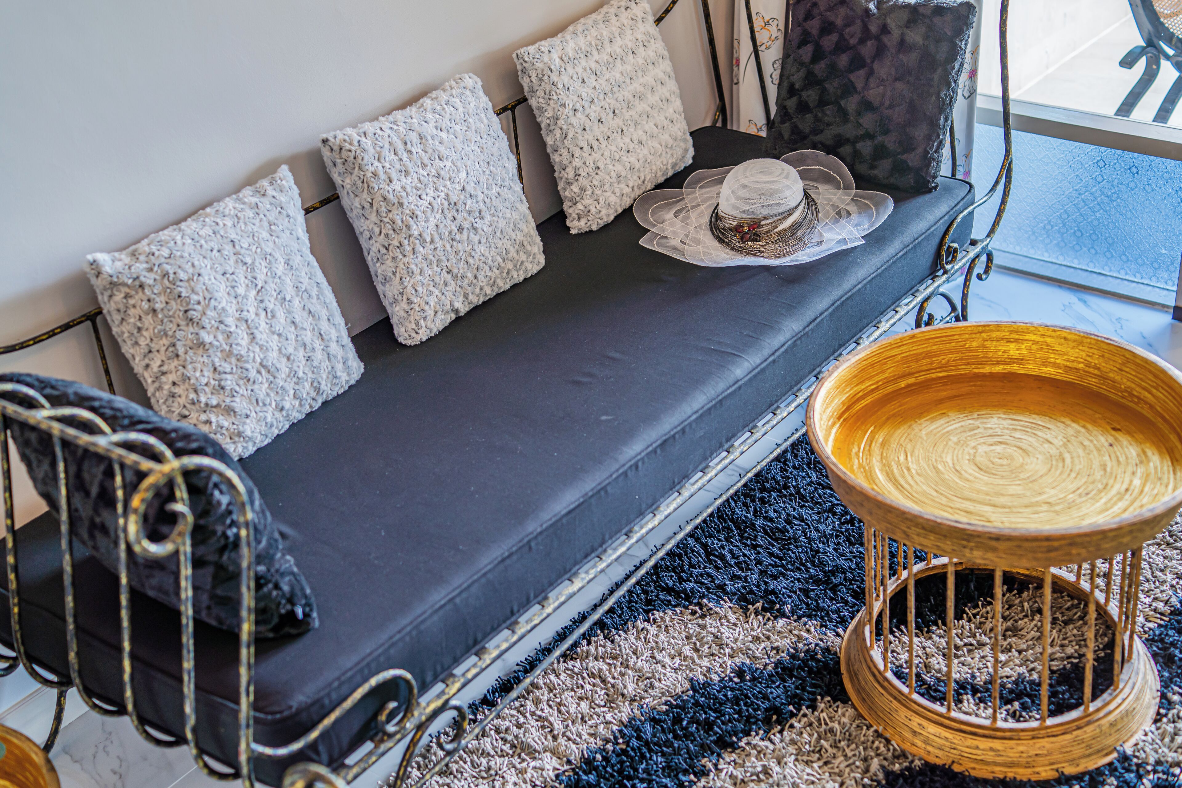 A dark-colored sofa with four textured pillows, a wicker side table, and a patterned rug.