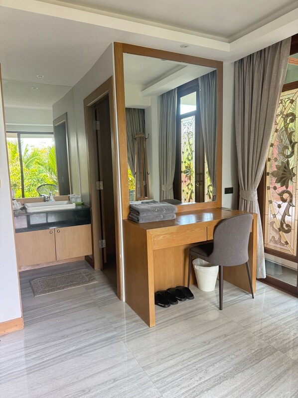 A modern bedroom with a wooden desk, a chair, a large mirror, and a view of the outdoors. - Bell Seaside Luxury Villa (Rawai)