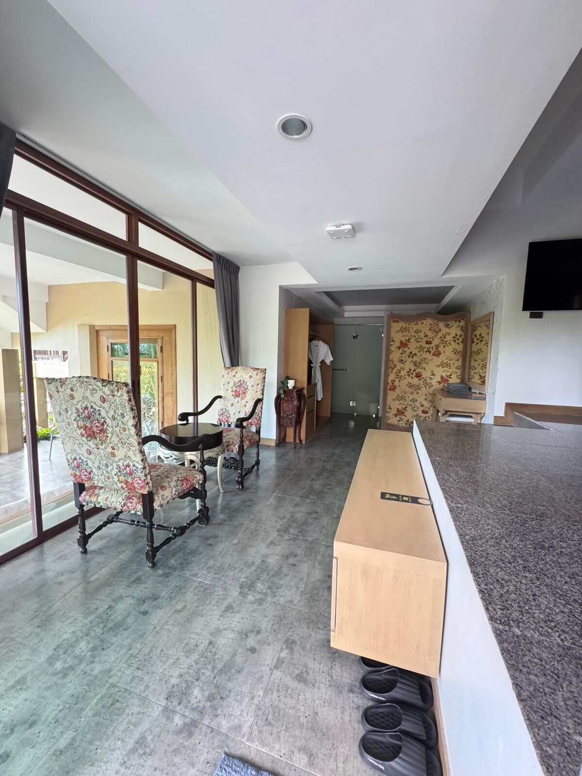Een moderne hotelkamer met een grote schuifglazen deur, een houten bankje en een flatscreen televisie aan de wand bevestigd.