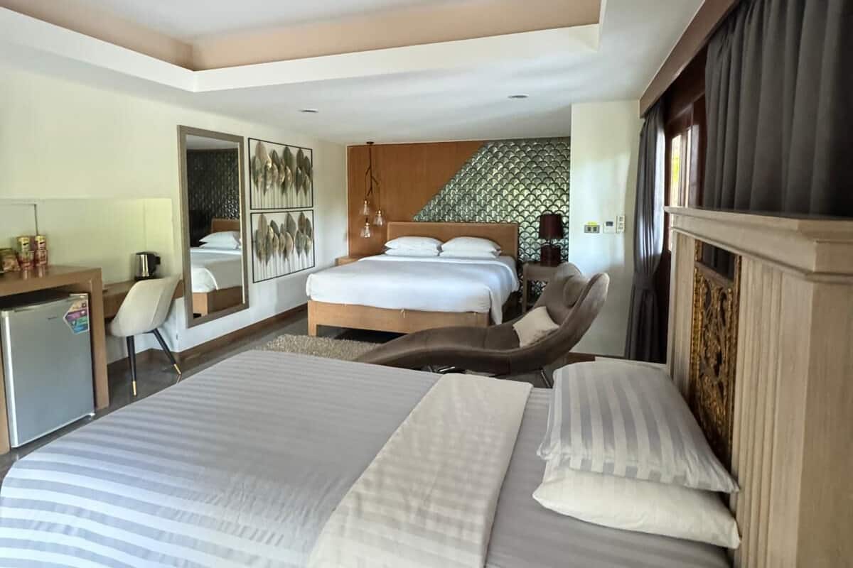 A hotel room with a large bed, a desk, a chair, and a small refrigerator.