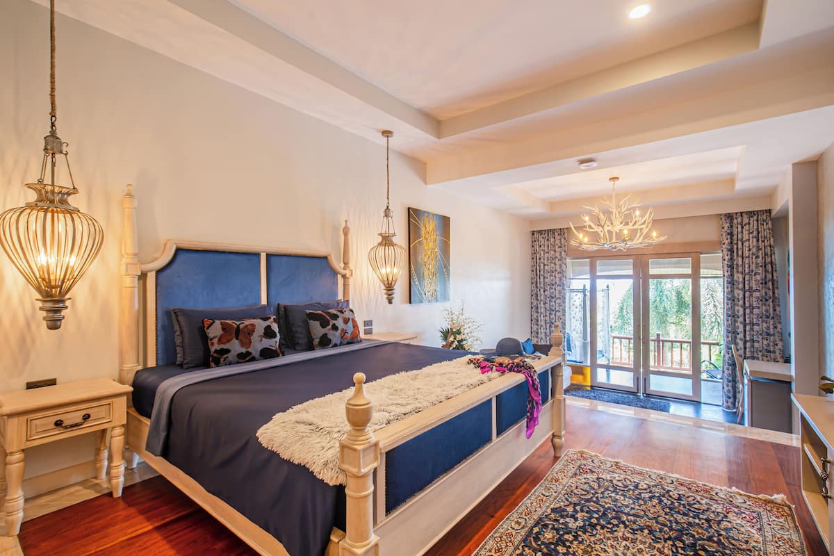 A bedroom with a large bed, two bedside tables, a chandelier, and a view of the outdoors.