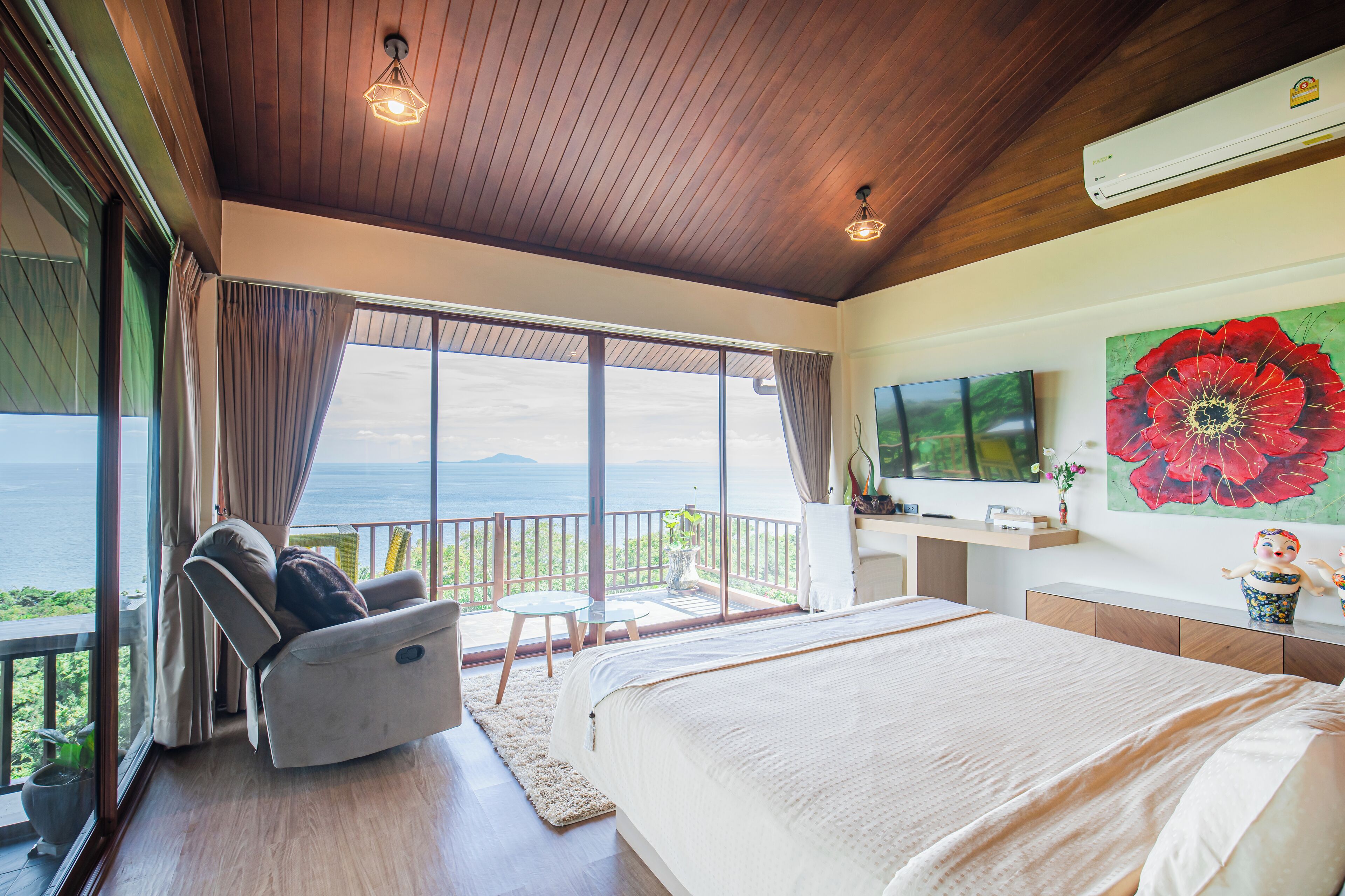 A bedroom with a large bed, a TV, a desk, and a view of the ocean.