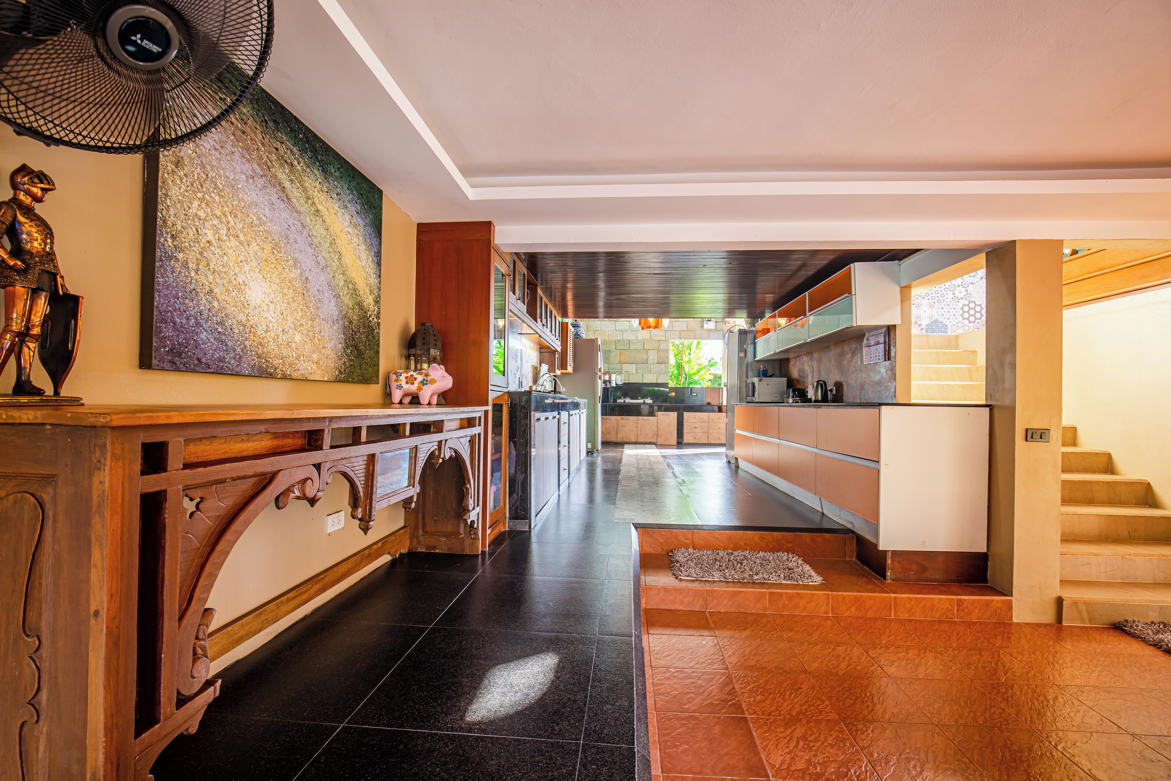 A spacious hallway with a wooden console table, a large abstract painting, and a staircase leading to an upper level.