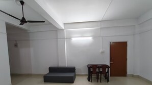A spacious room with a ceiling fan, a dark sofa, a small table with two chairs, and a door. - Jironi Residency In (Guwahati)