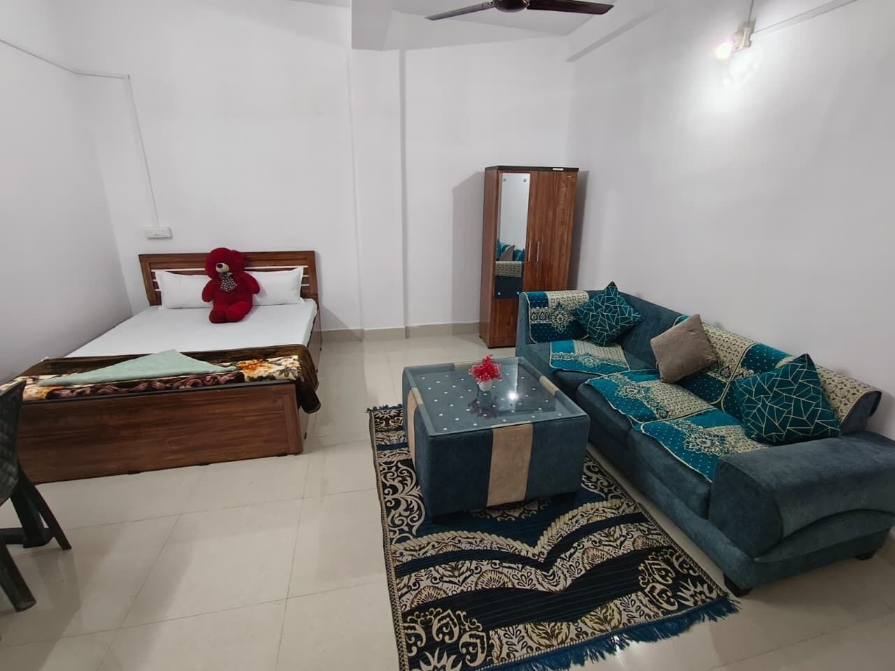 A room with a bed, a sofa, a coffee table, a mirror, and a ceiling fan.