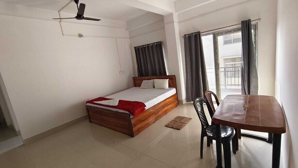 A bedroom with a bed, a ceiling fan, a window with curtains, and a dining table with chairs. - Jironi Residency In (Guwahati)