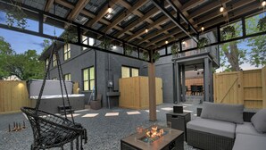 Eine Terrasse im Freien mit Feuerstelle, Korbmöbeln und einer Hängemattenliege.