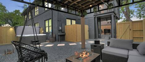 Une terrasse extérieure avec un foyer, des meubles en osier et un fauteuil suspendu.