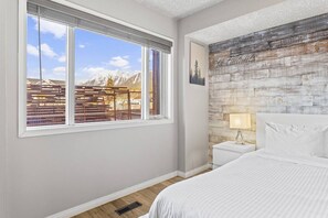 Une chambre avec une grande fenêtre, un lit, une table de chevet et un mur au style rustique.
