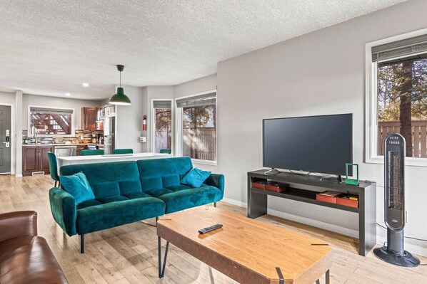 Un salon moderne avec un canapé de couleur turquoise, une table basse en bois et un téléviseur à écran plat posé sur un meuble noir.