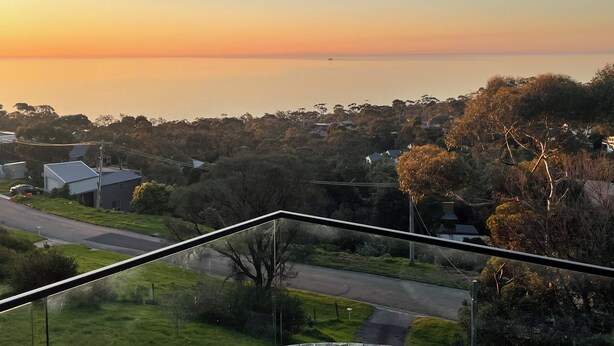 Zona residencial con casas, una carretera y vista al mar al atardecer.