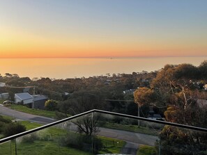 A residential area with houses, a road, and a view of the sea at sunset. - Modern Oceanview luxury. Tranquil heaven. Just minutes to the beach. (McCrae)