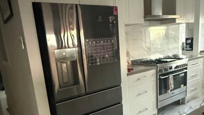 Una cocina moderna con electrodomésticos de acero inoxidable, armarios blancos y piso de mármol.