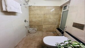 Un baño pequeño con inodoro, ducha y lavamanos. Hay un perchero con una toalla colgada.