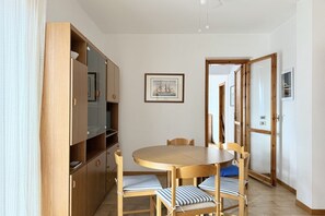 Un coin repas avec une table ronde en bois, quatre chaises dotées de coussins à rayures, un buffet en bois avec des étagères ouvertes et un tableau encadré accroché au mur.