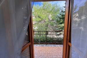 Een balkon met een metalen hekwerk, uitzicht op bomen en een gebouw op de achtergrond.