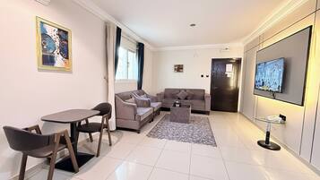 A modern living room with a sofa set, a dining table with chairs, a TV mounted on the wall, and a patterned rug.