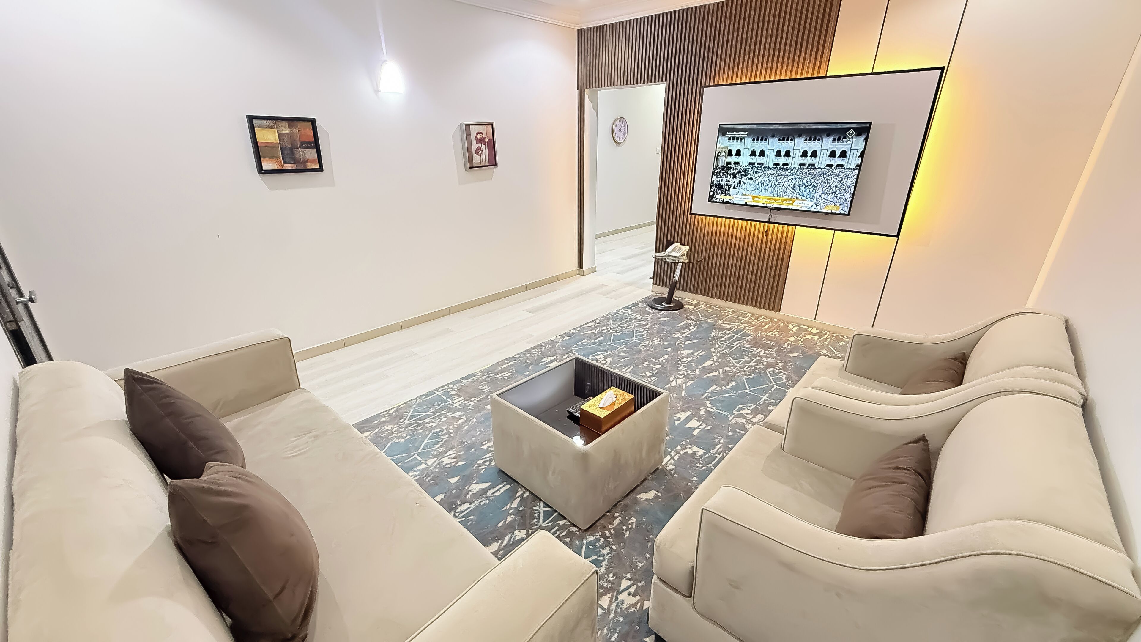 Ein modernes Wohnzimmer mit einer Couch, Sesseln, einem Couchtisch und einem flachbildfernseher an der Wand.