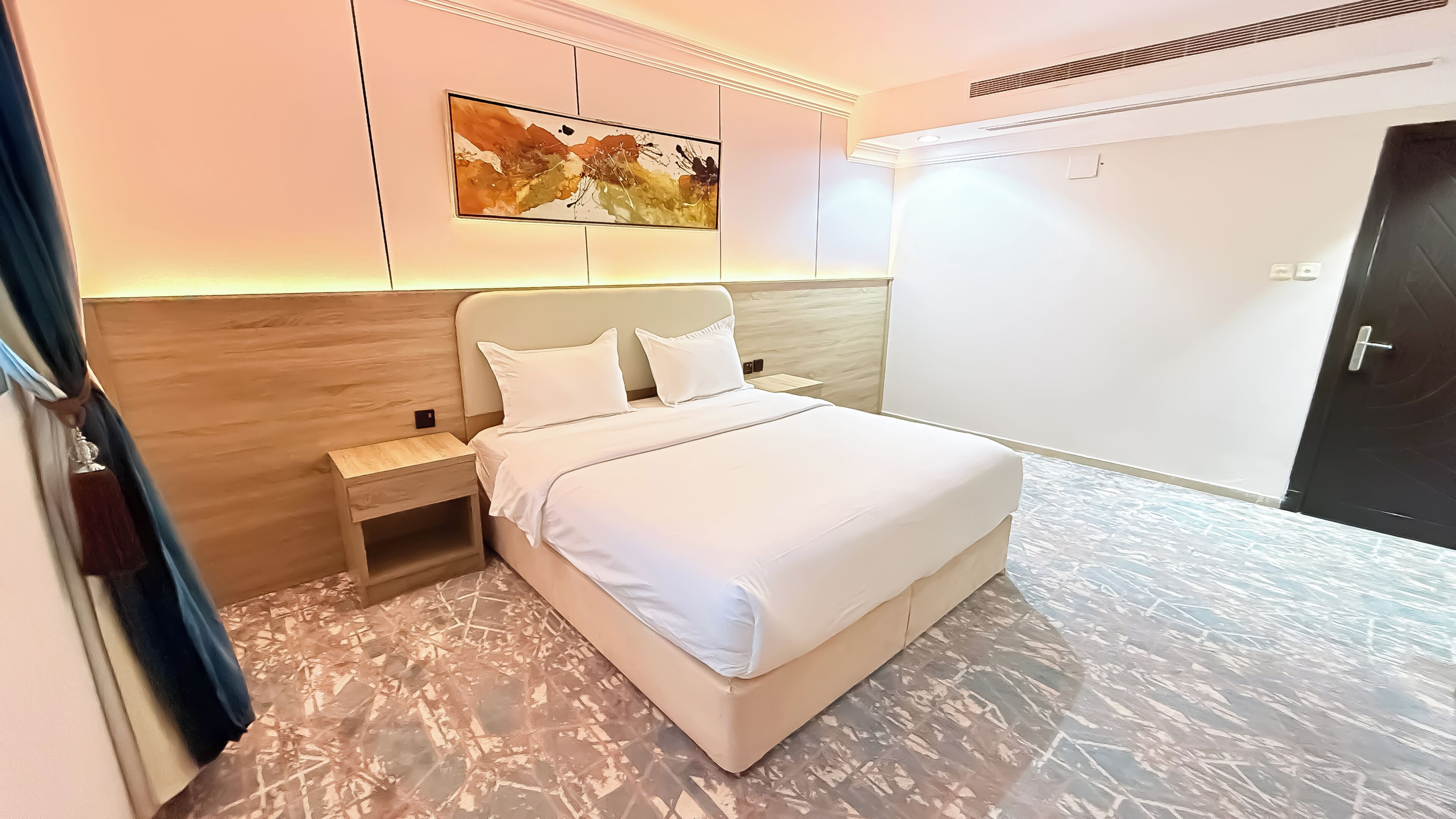 A modern hotel room with a bed, nightstand, and a painting on the wall.