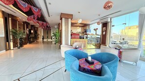 A hotel lobby with a modern design, featuring a reception desk, seating area with blue chairs, and large windows offering a view of the city.