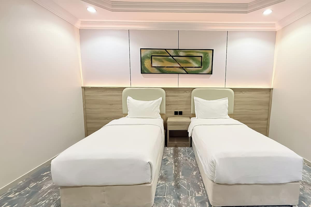 A hotel room with two single beds, a wooden headboard, a flat-screen TV mounted above the beds, and a marble floor.
