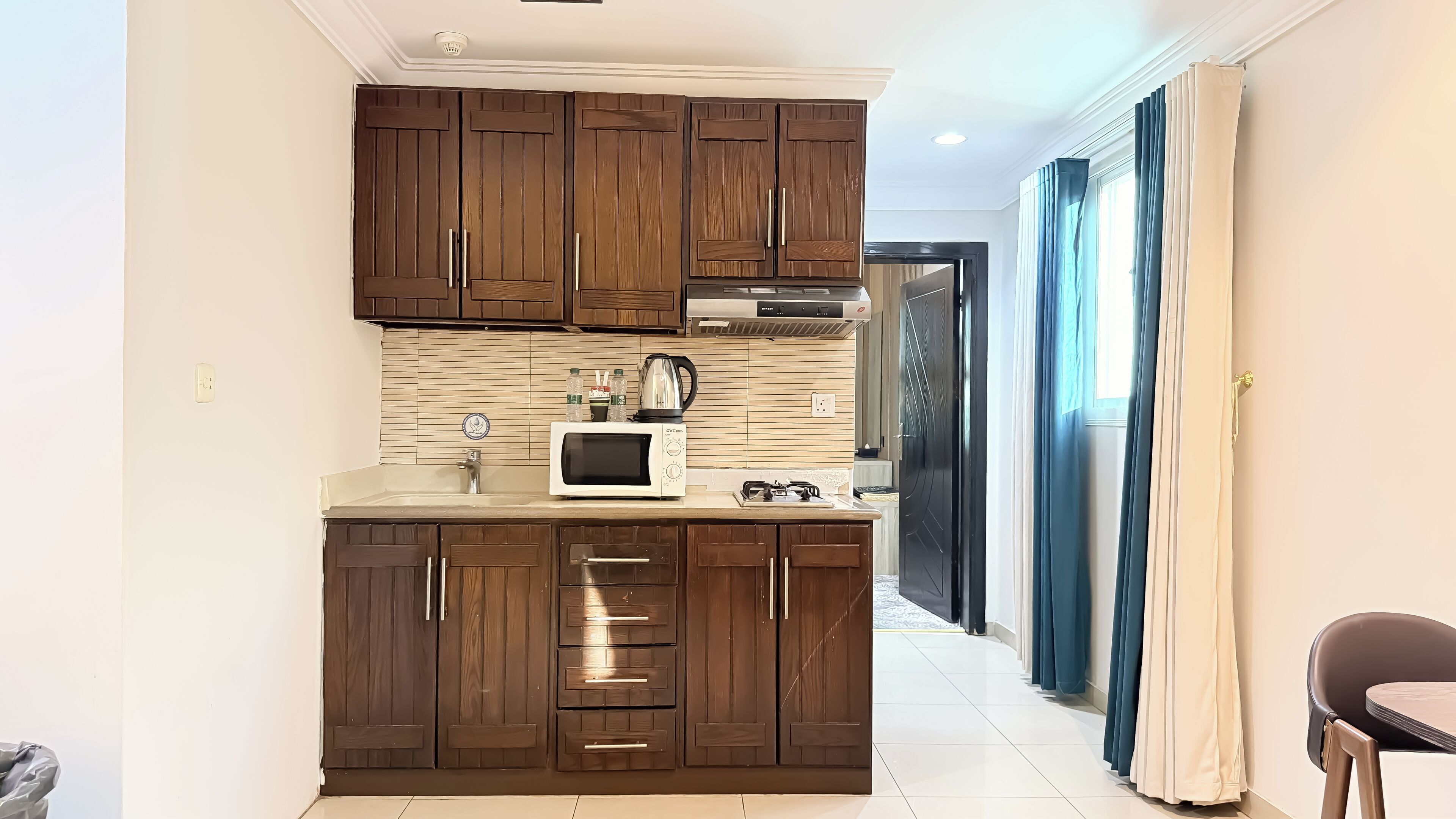 A compact kitchen with wooden cabinets, a microwave, a kettle, and a gas stove.