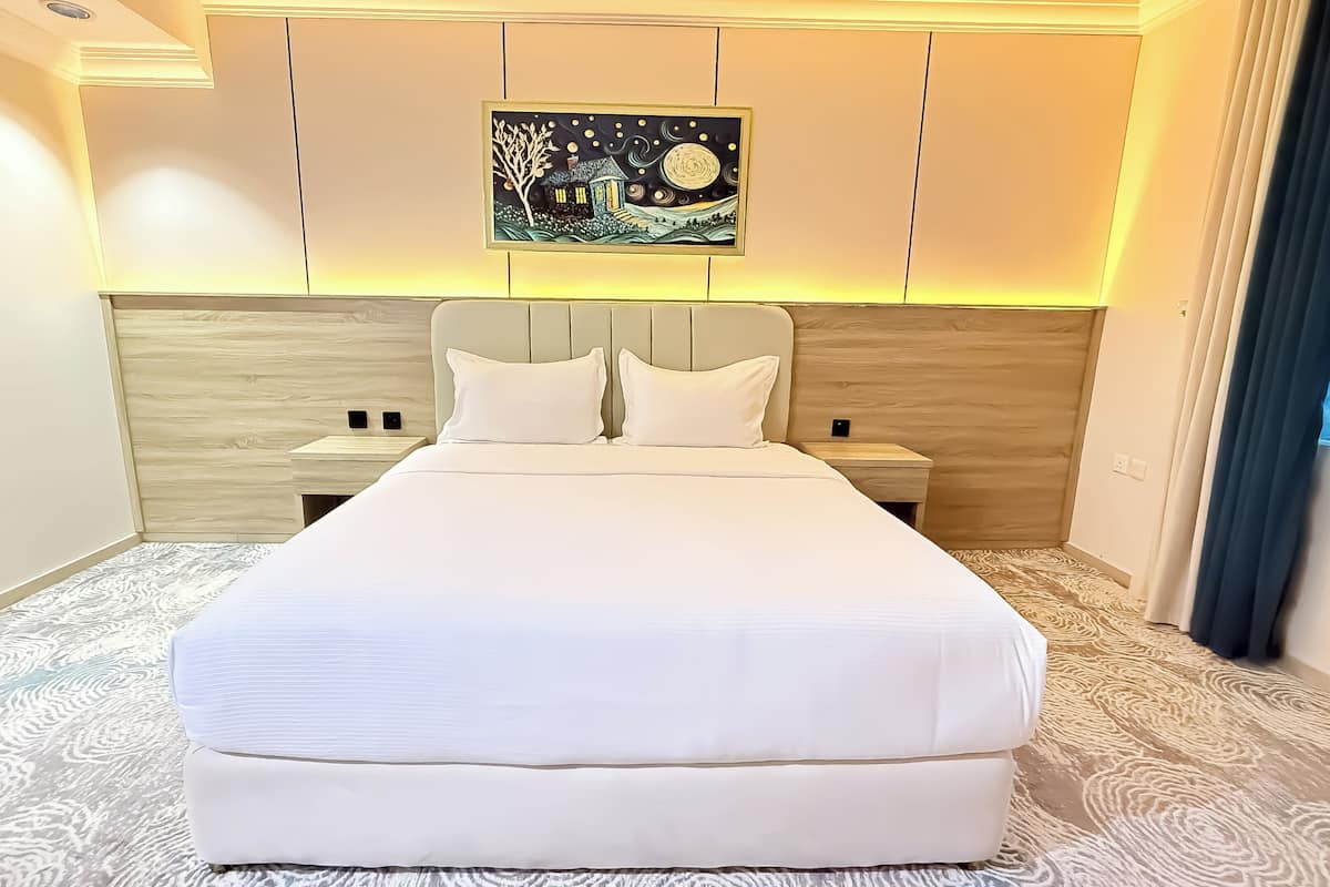 A modern hotel room with a large bed, two bedside tables, a nightstand, and a painting on the wall.