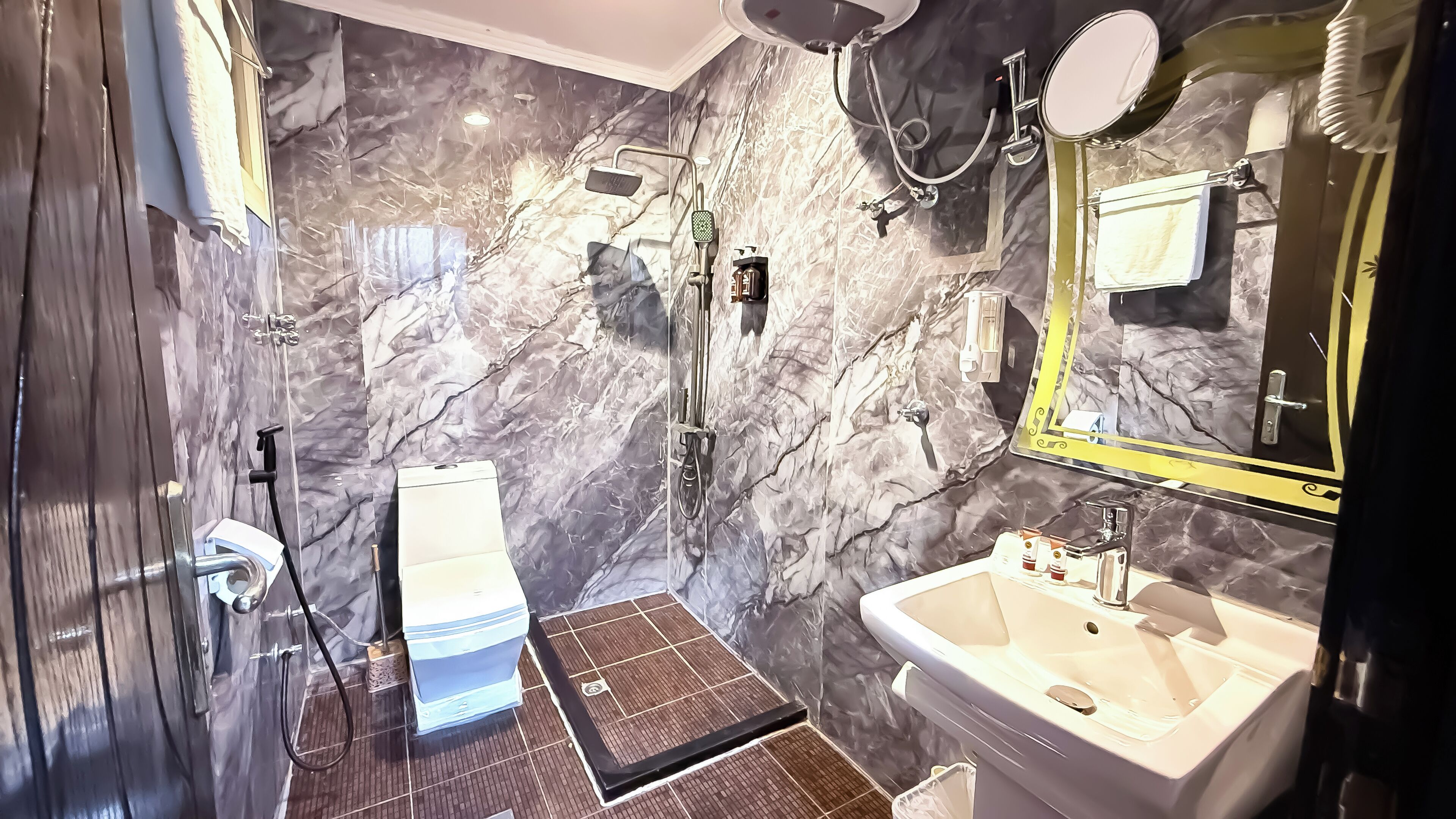 A modern bathroom with a marble wall, a large mirror, a sink, and a shower area.