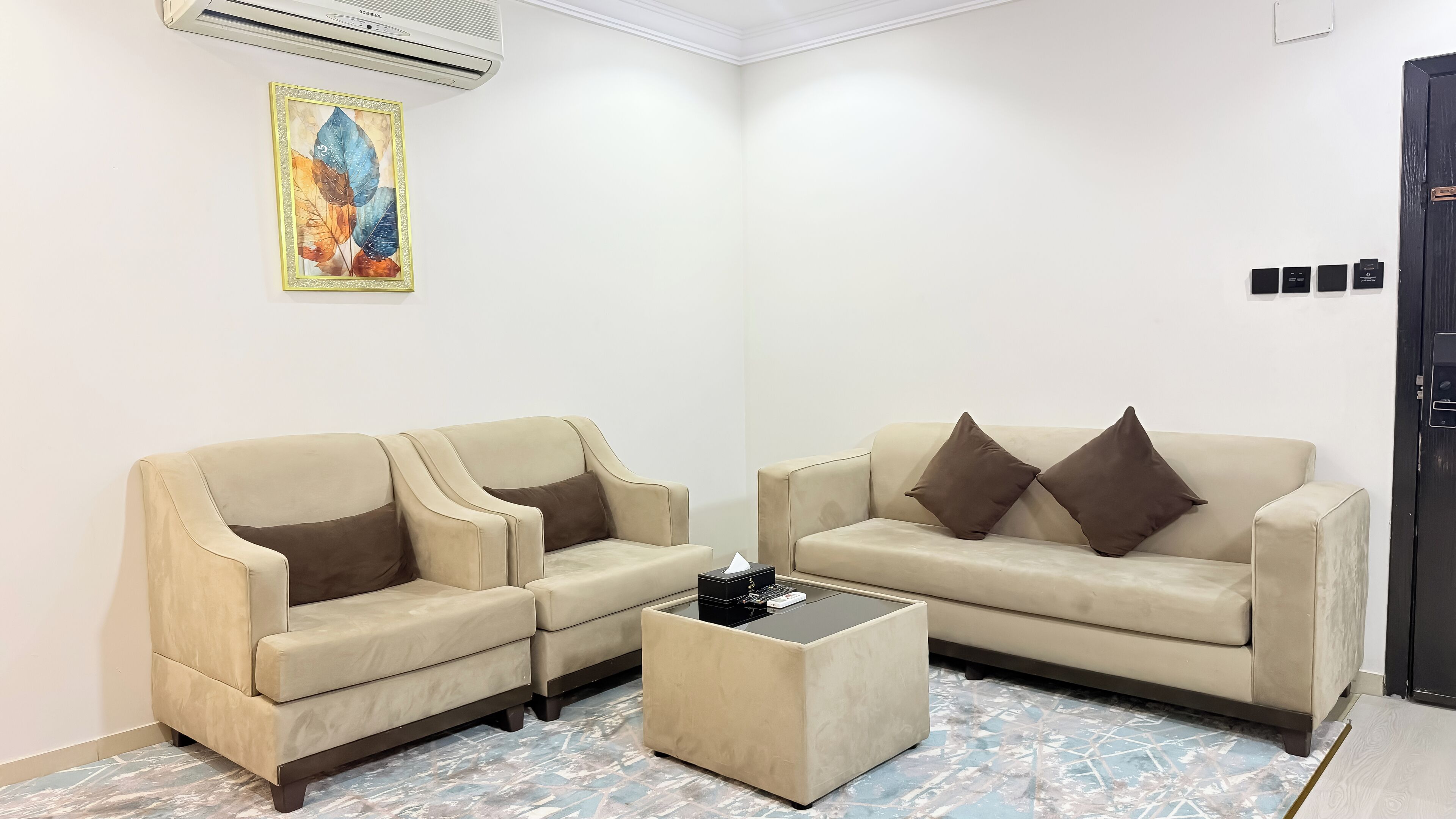 A room with two beige sofas, a small coffee table, a wall-mounted air conditioner, and a door with a lock.