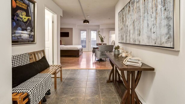 Een moderne woonkamer met een groot abstract schilderij, een houten salontafel en een bank met een hondentandpatroon.
