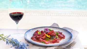 A dining table with a plate of food, a glass of red wine, and a pool in the background.
