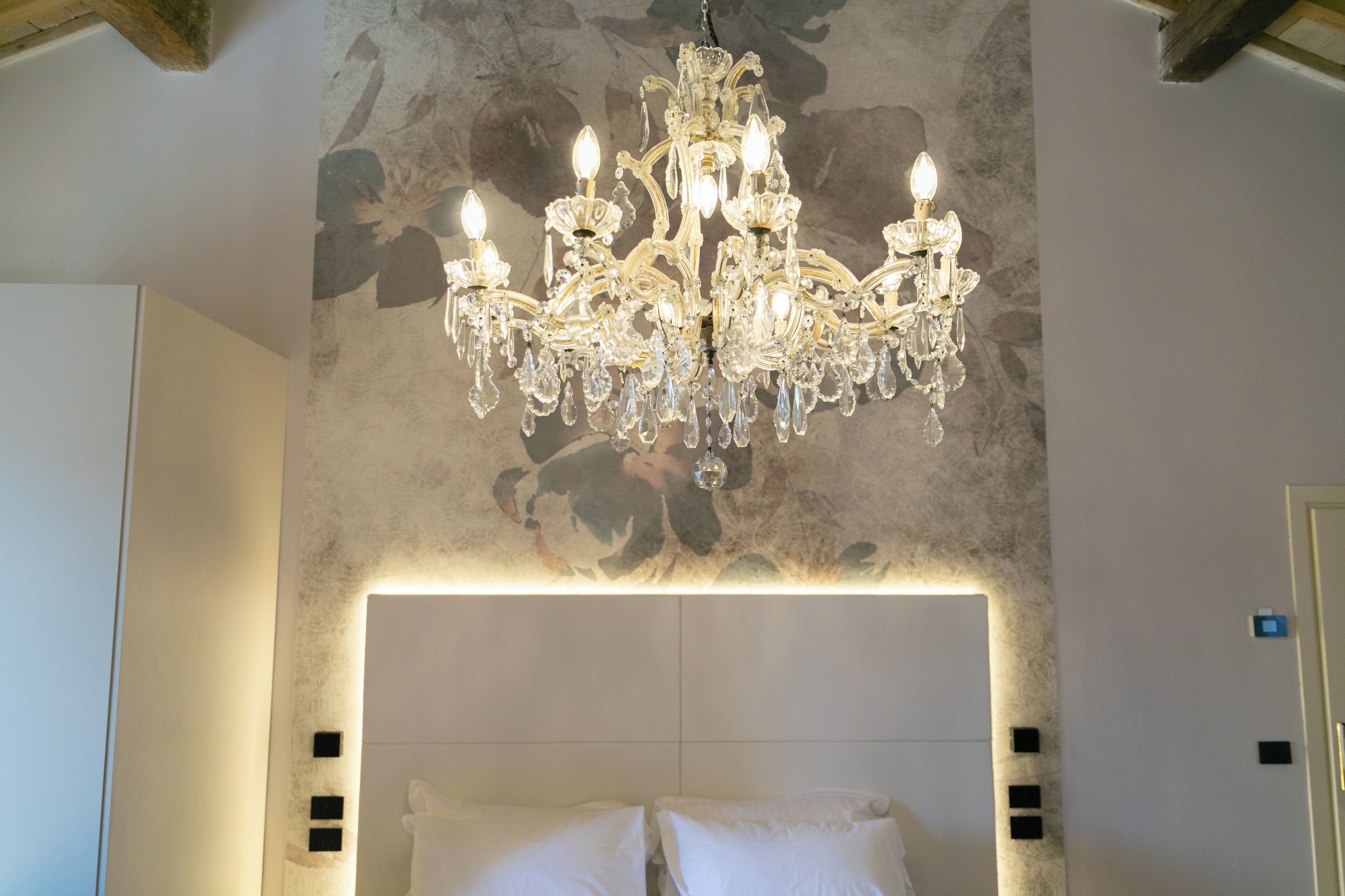 Un dormitorio con una gran araña ornamentada, un cabecero moderno y una pared con textura.