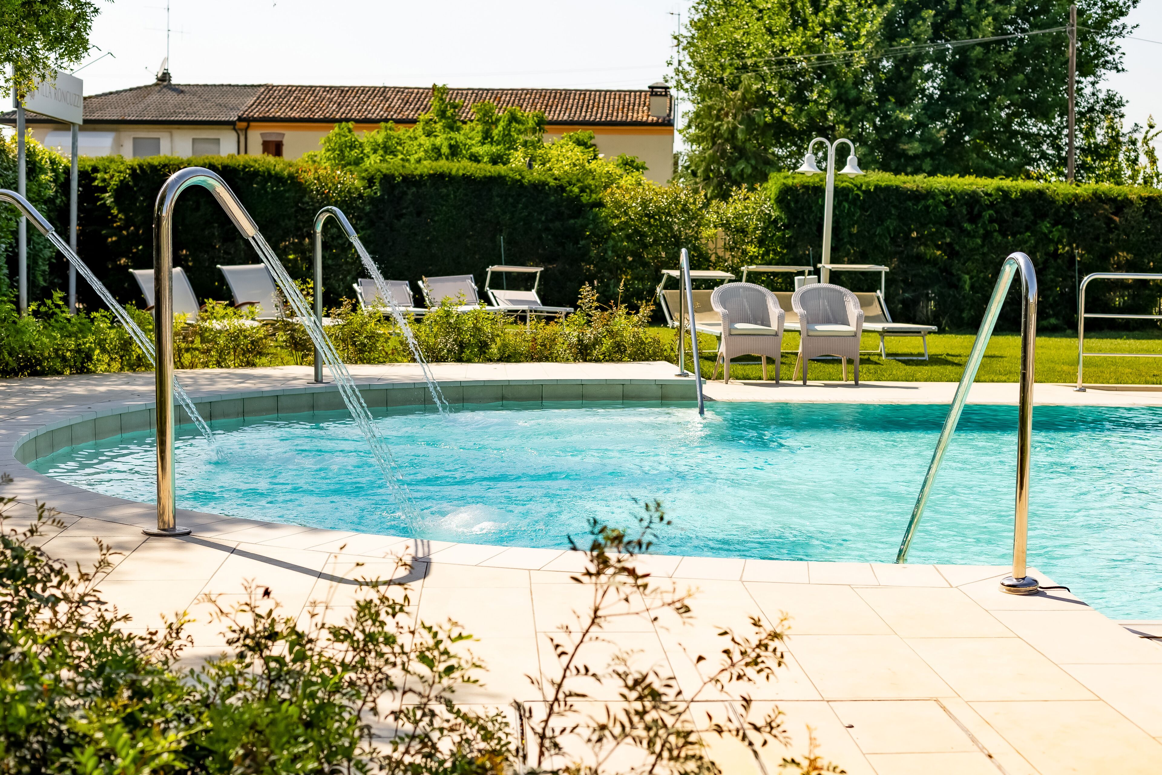 Una piscina con ringhiere in metallo, lettini e solarium piastrellato.