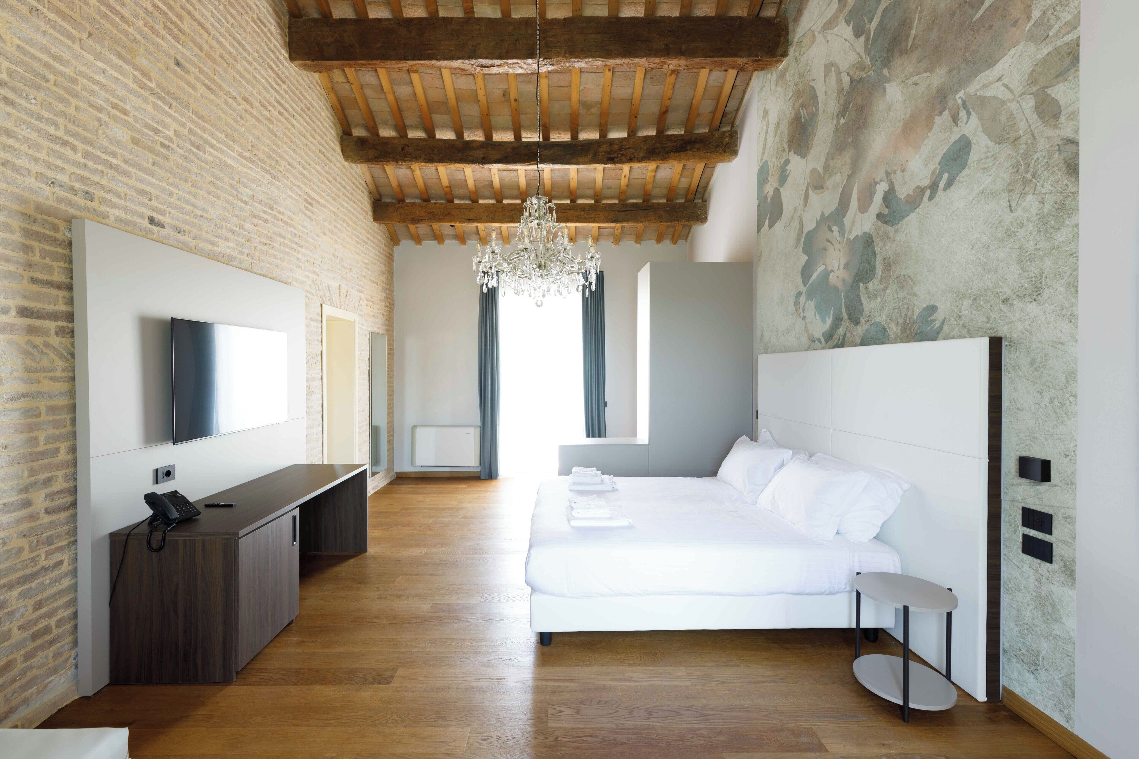 A modern bedroom with a large bed, a desk, a TV, and a chandelier.