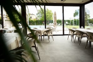 Un espace repas avec des tables et des chaises, une piscine et une vue sur l’extérieur.
