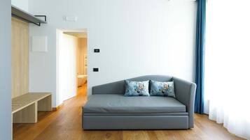 Een moderne woonkamer met een grijze bank, twee decoratieve kussens, een houten bankje en uitzicht op een badkamer door een open deur.