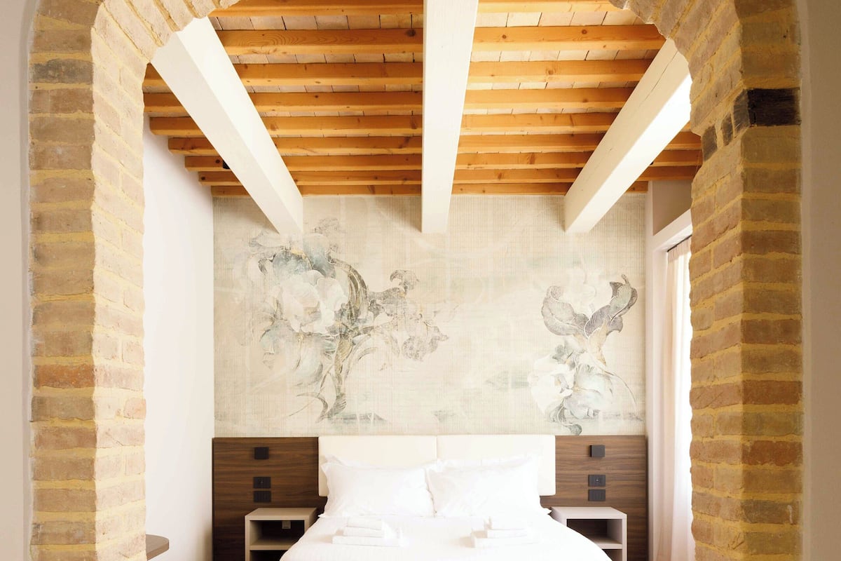 Un dormitorio con una cama grande, vigas de madera, paredes de ladrillo y un cuadro en la pared.