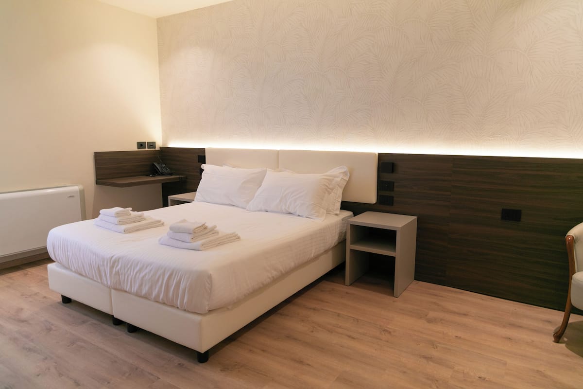A modern hotel room with a large bed, bedside tables, a wooden headboard, and a built-in shelf.