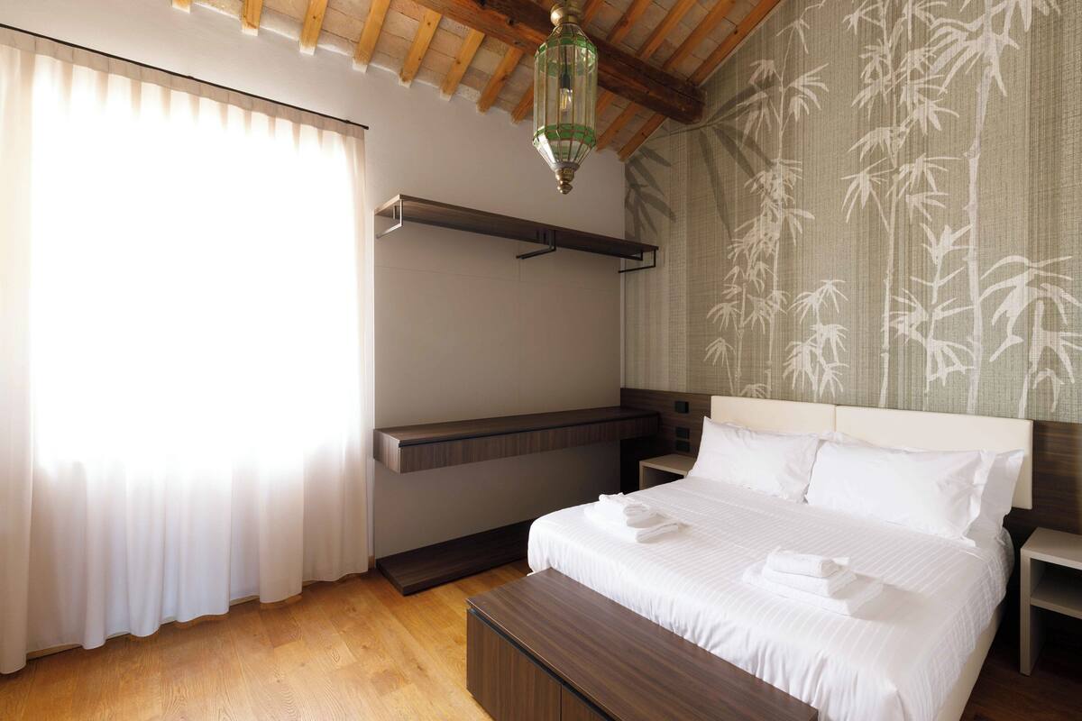 A hotel room with a bed, bedside table, and a hanging light fixture.
