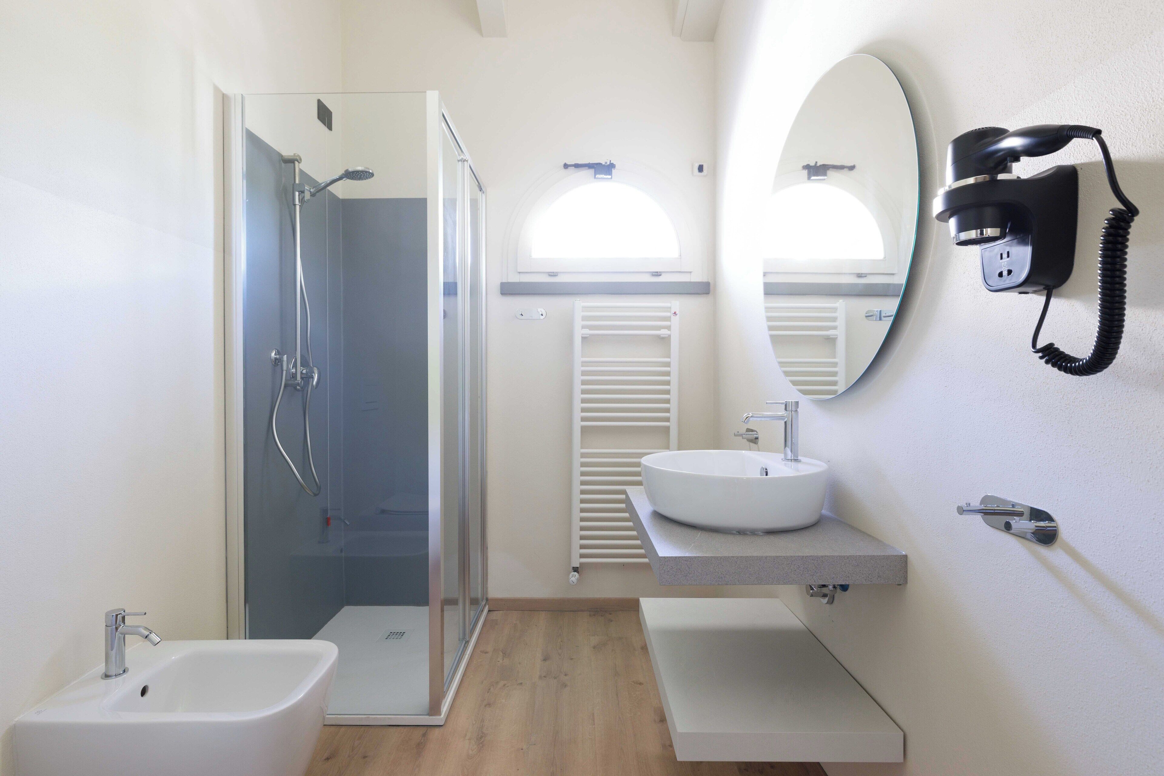 Un baño moderno con ducha de vidrio, lavamanos blanco y un bidé.