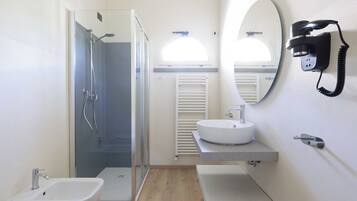 Un baño moderno con ducha de vidrio, lavamanos blanco y un bidé.