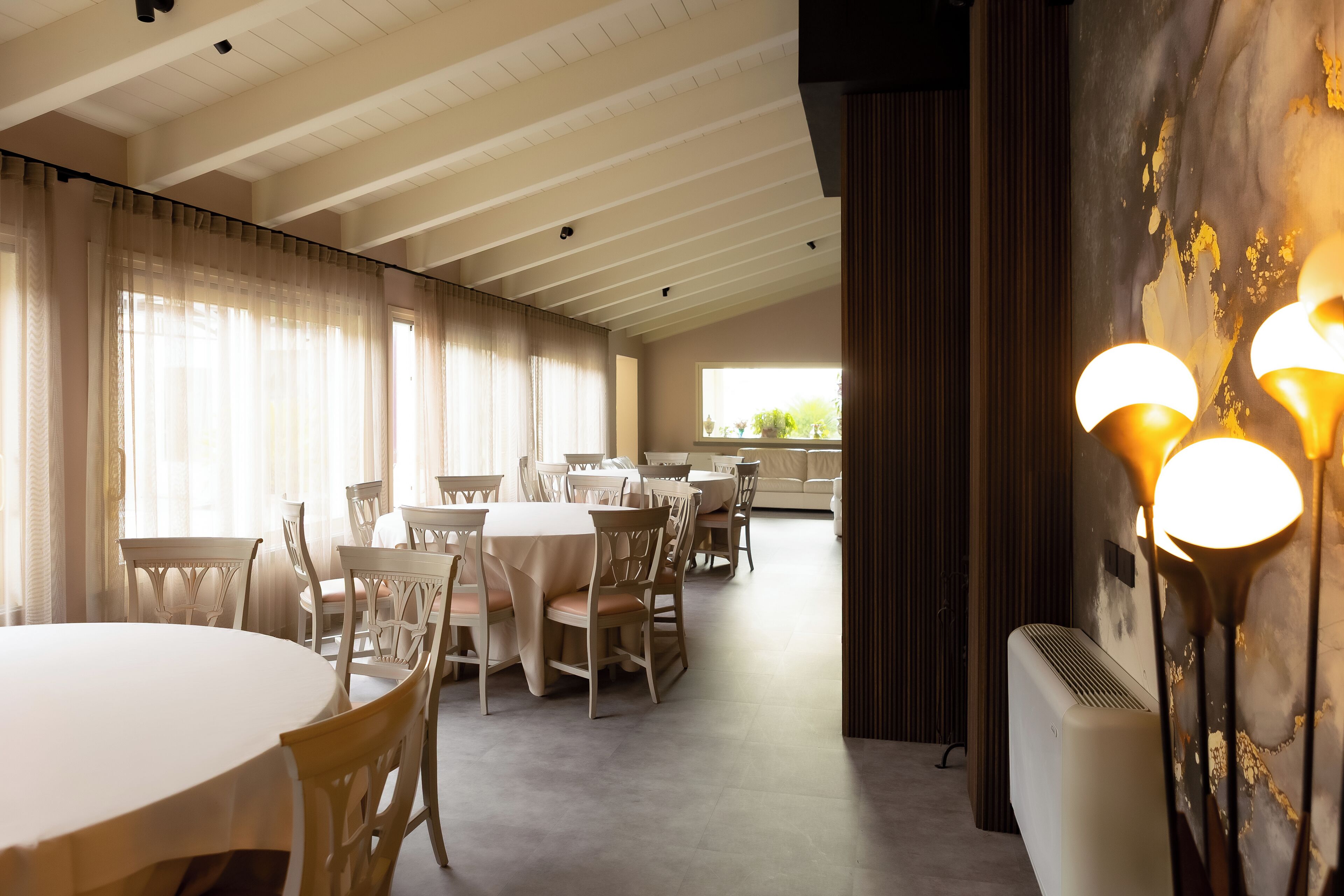 A dining area with round tables and chairs, a ceiling with exposed beams, and a wall-mounted air conditioning unit.