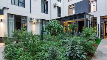 Une cour intérieure agrémentée de plantes en pot, une entrée avec une porte vitrée et un bâtiment doté de nombreuses fenêtres et de plusieurs unités de climatisation.